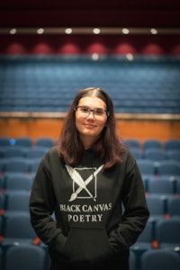 a woman in a black hoodie standing in front of an auditorium