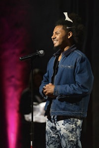 a man in a denim jacket is smiling into a microphone