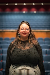 a woman in glasses standing in an auditorium